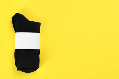 Pair of black cotton socks on yellow background, top view. Space for text