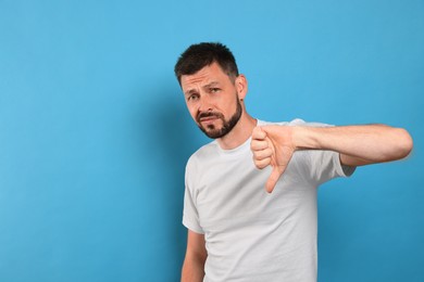 Man showing thumb down on light blue background, space for text