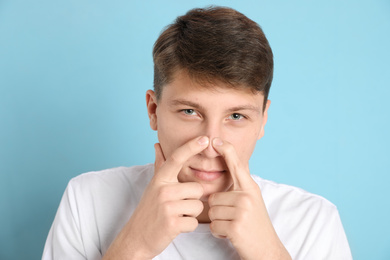 Photo of Teen guy with acne problem squeezing pimple on light blue background