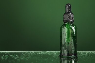 Bottle of face serum on wet surface against green background, closeup. Space for text