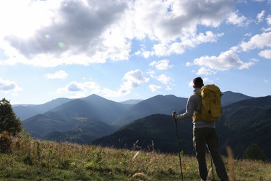 Tourist with backpack and trekking poles enjoying mountain landscape, back view. Space for text