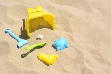 Photo of Bright plastic bucket, rake and shovel on sand. Beach toys. Space for text