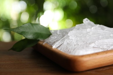 Menthol crystals and green leaves on wooden table against blurred background, closeup