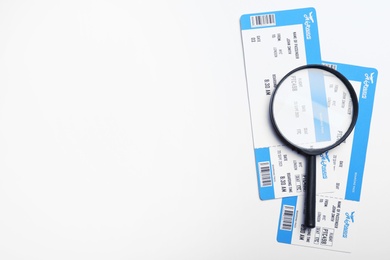 Avia tickets and magnifying glass on white background, flat lay with space for text. Travel agency concept