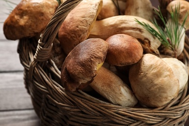Photo of Fresh wild mushrooms in wicker basket on wooden table, closeup