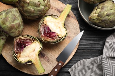 Cut and whole fresh raw artichokes on black wooden table, flat lay