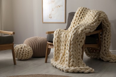 Soft chunky knit blanket on armchair in room. Interior design