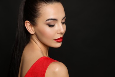 Portrait of young woman wearing beautiful red lipstick on black background, space for text