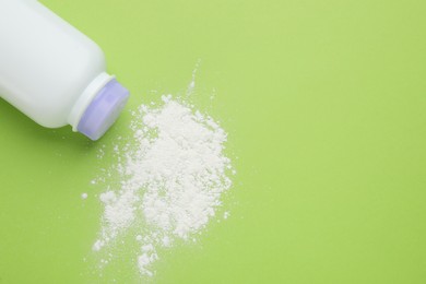Photo of Bottle and scattered dusting powder on light green background, top view with space for text. Baby cosmetic product