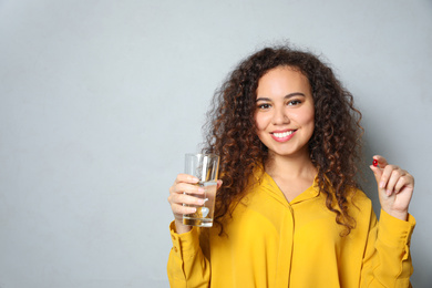 African-American woman with glass of water and vitamin capsule on light grey background. Space for text