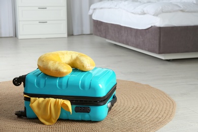 Suitcase with clothes and travel pillow in bedroom