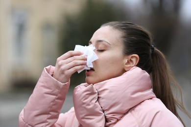 Ill woman with paper tissue sneezing outdoors