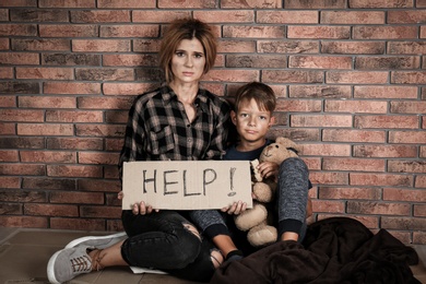 Poor woman with her son asking for help near brick wall