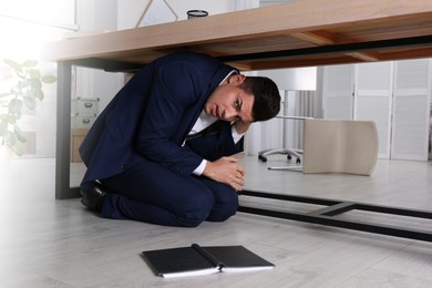 Scared man hiding under office desk during earthquake