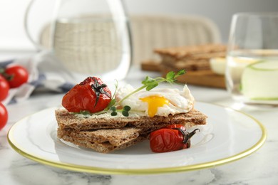 Fresh rye crispbreads with poached egg, cream cheese and grilled tomatoes on white marble table, closeup
