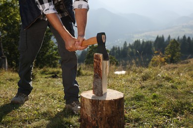 Man with axe cutting firewood in mountains, closeup