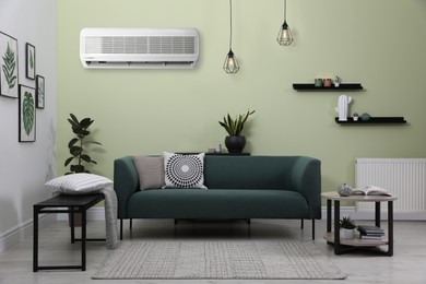 Modern air conditioner on light green wall in living room with stylish furniture
