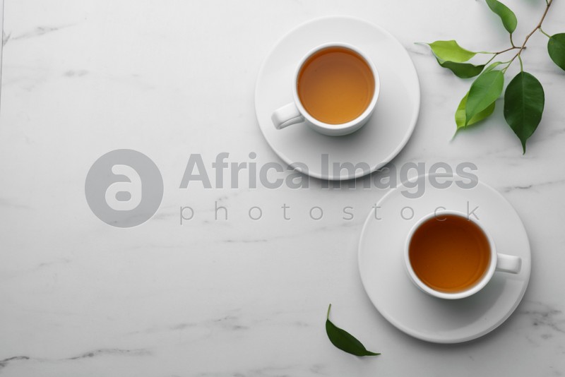 Photo of Green tea in cups with leaves on white marble table, flat lay. Space for text