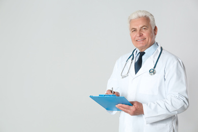Portrait of senior doctor with clipboard against light background