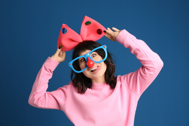 Emotional woman with funny glasses and large bow on blue background. April fool's day