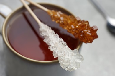 Sticks with sugar crystals and cup of tea on table, closeup