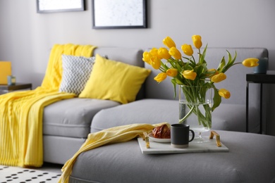 Tray with beautiful tulips on sofa indoors. Interior design in grey and yellow colors