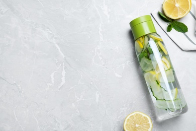 Bottle of refreshing water with cucumber, lemon and mint on light grey table, flat lay. Space for text