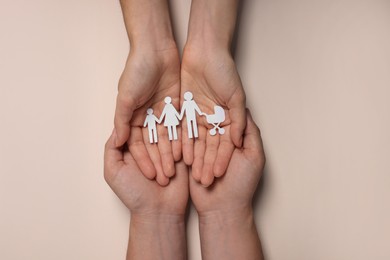 Couple holding paper family figures on beige background, top view. Insurance concept