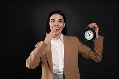 Emotional businesswoman holding alarm clock on black background. Time management