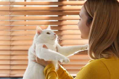 Young woman with her beautiful white cat near window at home. Fluffy pet