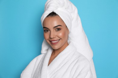 Beautiful young woman wearing bathrobe and towel on head against light blue background