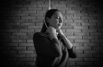 Depressed woman with rope noose on neck near brick wall. Suicide concept