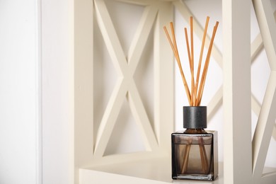 Photo of Aromatic reed freshener on wooden shelf indoors, space for text