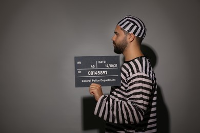 Prisoner in special uniform with mugshot letter board 
on grey background
