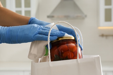 Woman cleaning newly purchased jar of pickled tomatoes with antiseptic wipe indoors, closeup. Preventive measures during COVID-19 pandemic