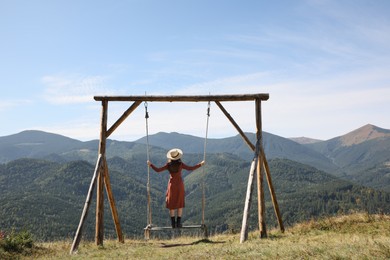 Photo of Young woman on outdoor swing in mountains, back view