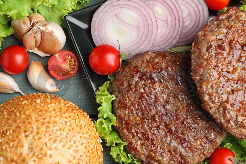 Grilled meat cutlets and ingredients for burger on blue wooden table, top view