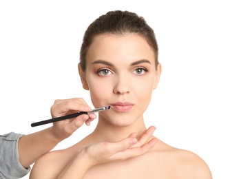 Visage artist applying makeup on woman's face against white background. Professional cosmetic products
