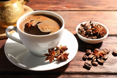 Photo of Aromatic hot coffee with anise stars and beans on wooden table