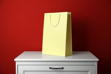 Paper shopping bag on white chest of drawers against red background