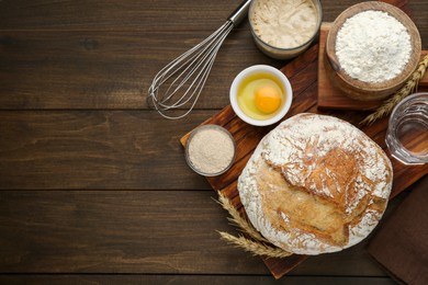 Photo of Freshly baked sourdough bread and ingredients on wooden table, flat lay. Space for text