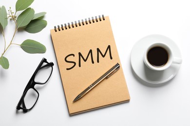 Notebook with abbreviation SMM, cup of coffee and glasses on white background, flat lay. Social media marketing