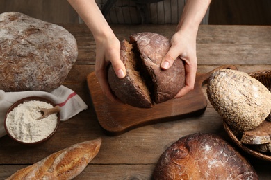 Woman breaking freshly baked bread at wooden table, closeup