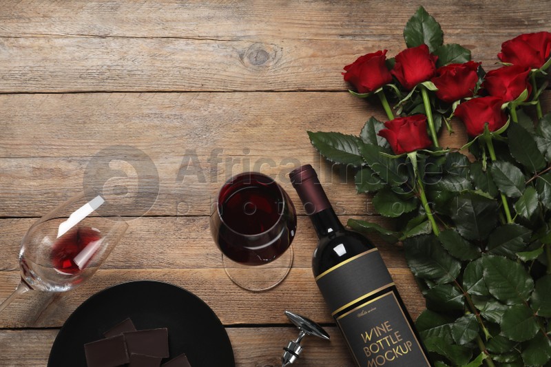 Photo of Bottle and glasses of red wine near beautiful roses on wooden table, flat lay. Space for text