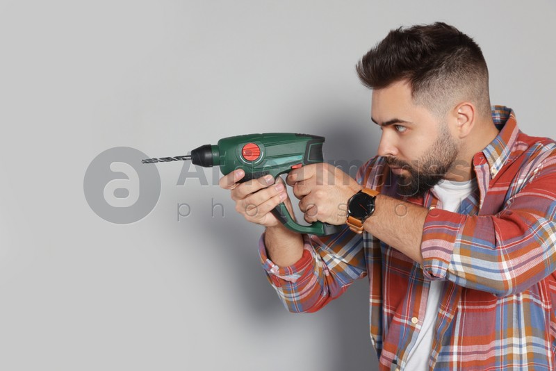 Young man with power drill on grey background