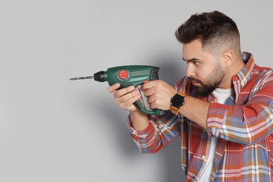 Young man with power drill on grey background