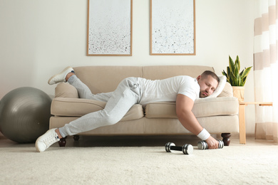 Lazy overweight man with dumbbells sleeping on sofa at home