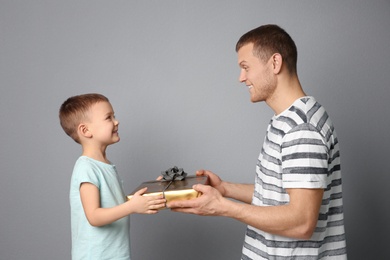 Man receiving gift for Father's Day from his son on grey background