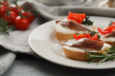 Photo of Delicious sandwiches with cream cheese, anchovies and tomatoes on grey wooden table, closeup. Space for text