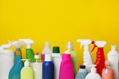Photo of Many bottles of different detergents on yellow background, space for text. Cleaning supplies